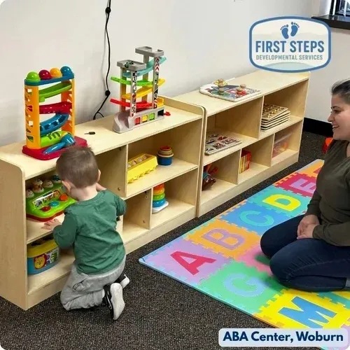 Child engaging with educational toys in an ABA therapy center, with a caregiver observing, highlighting individualized learning and skill development at First Steps Developmental Services, Woburn.