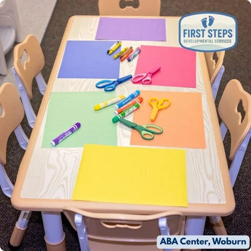 Table set up for play-based learning at First Steps Developmental Services, featuring colorful construction paper, scissors, and markers, in a nurturing environment designed for child-led exploration