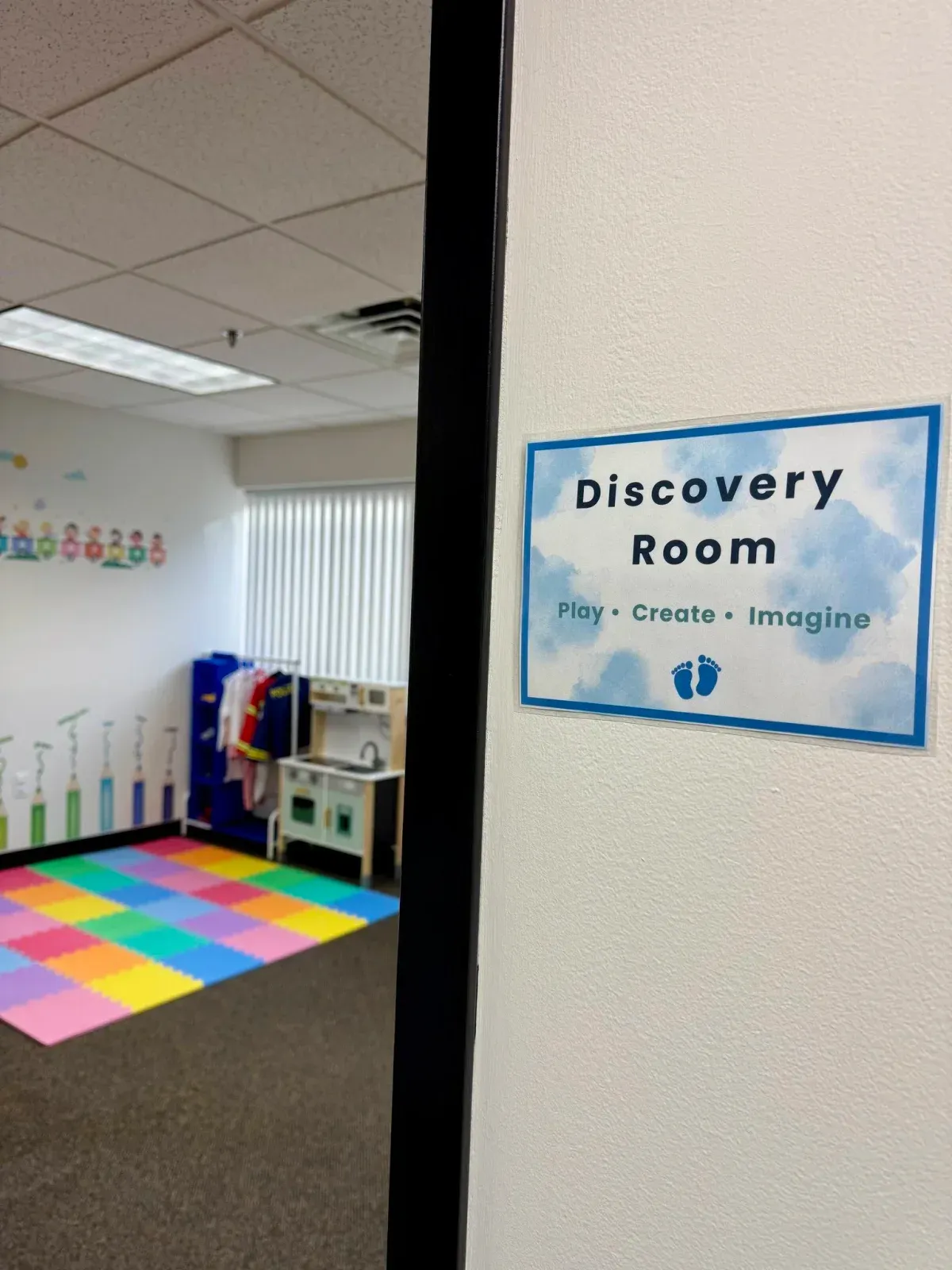 Discovery Room sign featuring playful colors and text inviting children to play, create, and imagine; colorful foam floor mats visible, enhancing the child-led learning environment at First Steps Developmental Services