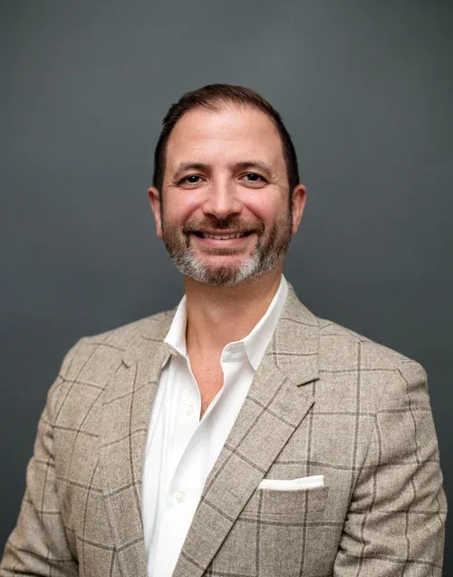 Jarrod Scalzo, MSEd, BCBA, LABA, smiling in a professional blazer, representing First Steps Developmental Services&rsquo; commitment to empowering children and families.