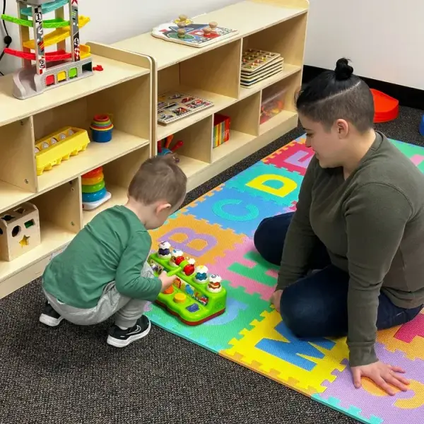 Child and therapist engaging in play-based ABA therapy with colorful toys on a foam mat, promoting developmental skills and learning in a supportive environment.